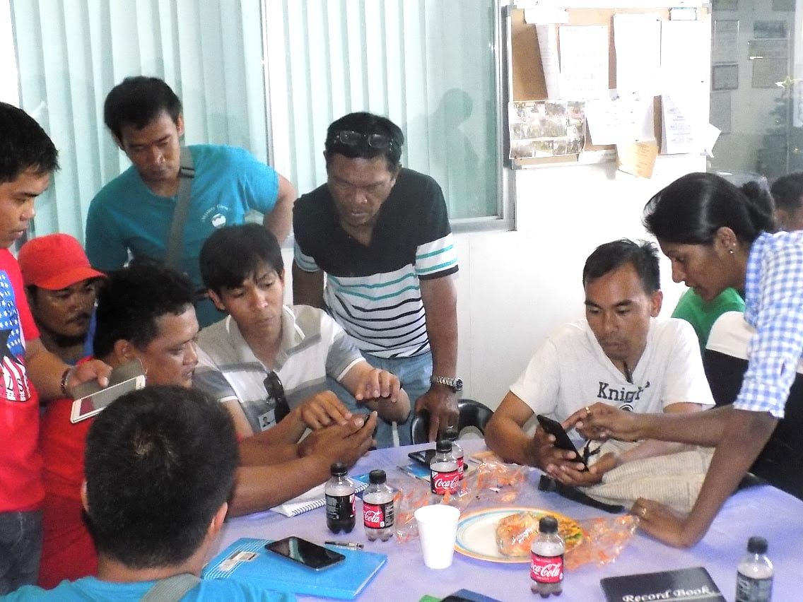 A field team seated around a table working through the seed production management app on their phones during a training session