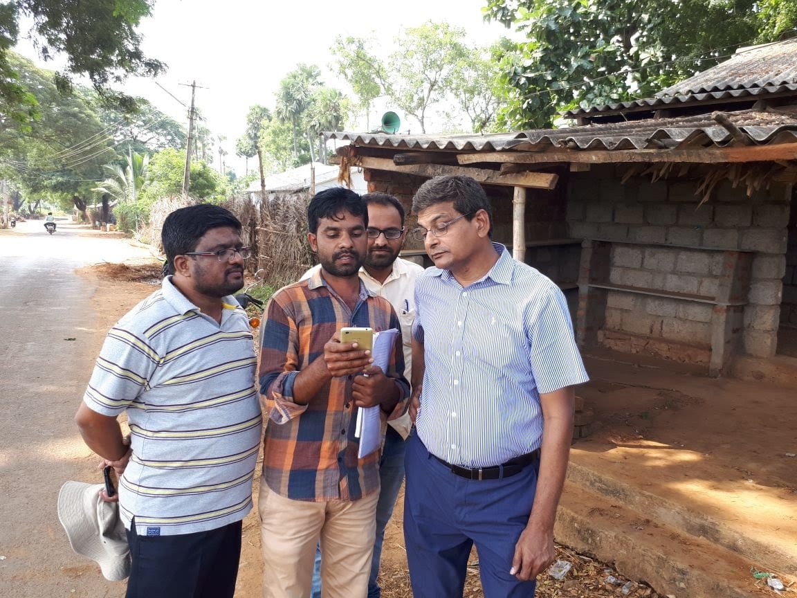 Four colleagues reviewing the corn seed production management system on a mobile phone at the roadside in a village